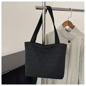 Close-up of black quilted puffer tote bag with wavy stitching hanging on a garment rack