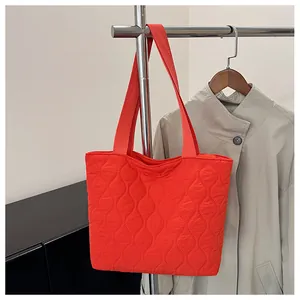 Close-up of bright orange quilted puffer tote bag with stylish wave pattern stitching
