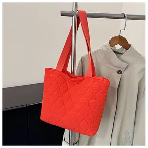 Detail of orange quilted tote bag with wave stitching and wide shoulder straps on display
