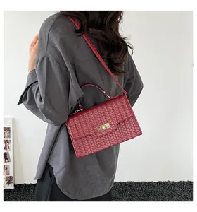 Detail view of burgundy woven texture handbag with golden clasp worn by a model