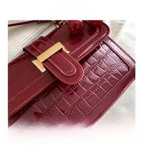 Détail du sac rouge foncé à texture crocodile avec boucle dorée et breloque cerise