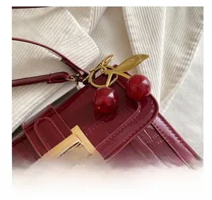 Détail de breloque cerise scintillante sur un sac en cuir bordeaux à motif crocodile