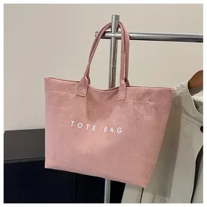 Detail of pink faux suede tote bag featuring white TOTE BAG text and dual handle design