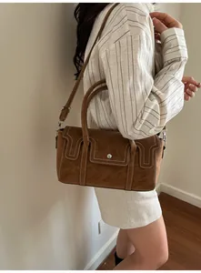 Close-up of brown suede small square bag with decorative white stitching and silver hardware