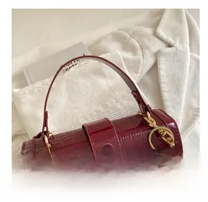 Détail d'un sac à main rouge vin en cuir verni avec motif crocodile et bijou cerise