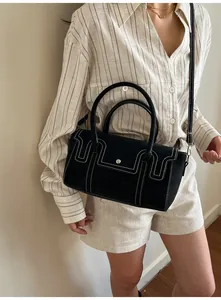 Detail of black suede-textured bag featuring white contrast stitching and round metal clasp