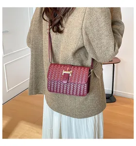 Detail van bordeauxrode geweven crossbodytas met een gouden H-vormige gesp