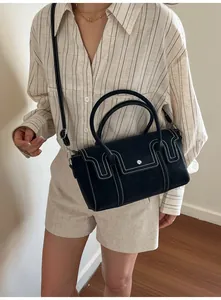 Detail of black crossbody bag featuring contrast white stitching and round metal handles