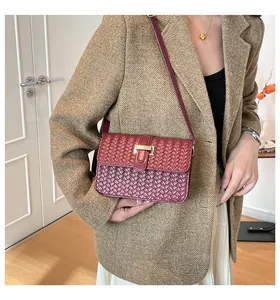 Detail van bordeauxrode gevlochten schoudertas met gouden sluiting op tweed jas