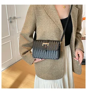 Detailopname van zwarte geweven crossbodytas met een elegante gouden metalen T-sluiting