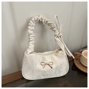 Dettaglio di borsa beige con texture a pieghe e fiocco in metallo dorato elegante