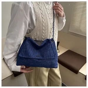 Détail d'un sac cabas en jean bleu avec bandoulière en chaîne et rabat de fermeture