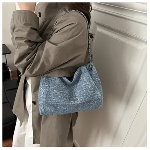 Détail d'un cabas en denim bleu avec bandoulière en chaîne et plaque carrée minimaliste