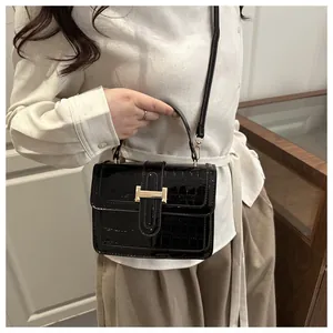 Détail du sac bandoulière en cuir vernis noir à motif crocodile et boucle dorée en H