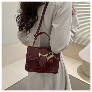 Détail d'un sac bandoulière bordeaux motif crocodile avec accessoire pendentif cerise