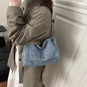 Grand sac cabas en denim bleu avec bandoulière chaîne porté à l'épaule par un mannequin