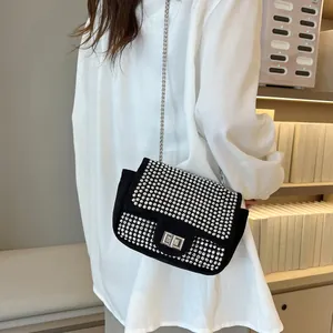 Detail of black suede shoulder bag with silver rhinestones and chain strap on model