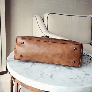 Bottom view of brown PU leather bag with metal feet on marble and fabric background