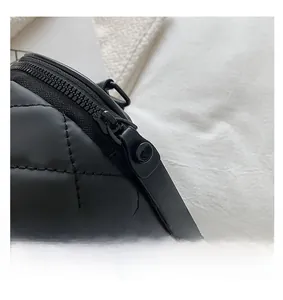 Close-up of the smooth black metal zipper and quilted diamond texture on the cylinder bag