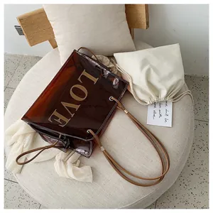 Close-up of brown transparent PVC tote bag with gold LOVE patch and cotton inner pouch