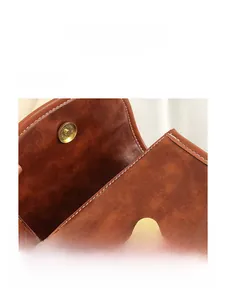 Détail du sac en cuir marron avec fermoir magnétique doré et surpiqûres blanches contrastées