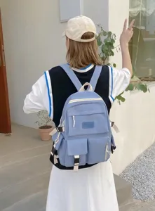 Outdoor street style view of a light blue multi-pocket canvas backpack for students