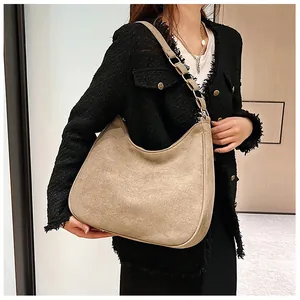 Beige suède hobo tas met brede schouderband en metalen ring gedragen door een model