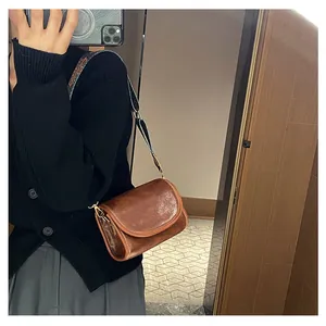 Sac bandoulière en cuir marron rétro avec large sangle tissée montré en selfie miroir