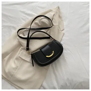 Close-up of black saddle bag with gold crescent buckle on beige blazer background