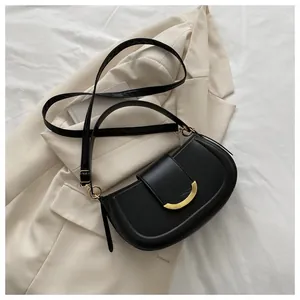Detail of a black crescent saddle bag with gold crescent hardware on white fabric
