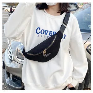 Outdoor street view of a black corduroy crossbody bag with golden zippers and strap