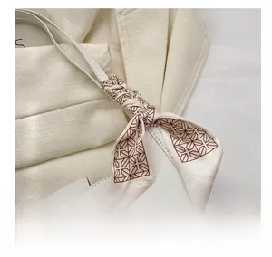 Detail of elegant beige silk scarf with brown patterns tied on a white handbag