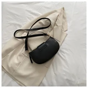 Close-up of black crescent saddle bag with gold hardware on a beige blazer background