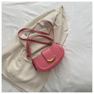 Detailed flat lay of pink saddle bag with golden crescent clasp on textured white fabric