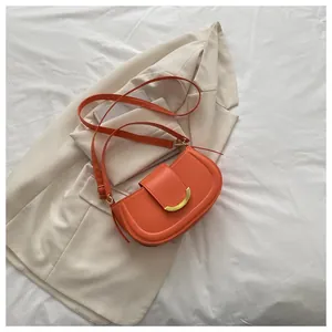 Detail shot of orange saddle bag with gold metal buckle on beige blazer background
