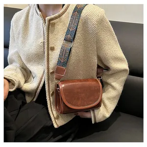 Détail d'un sac bandoulière vintage en cuir marron avec large sangle brodée
