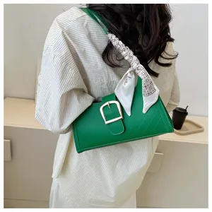 Detail of emerald green leather bag with gold buckle and silk scarf on handle