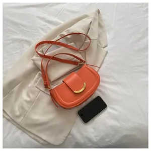 Detail of orange saddle bag with gold crescent buckle on beige blazer background