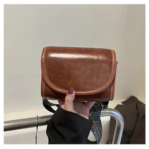 Détail d'un sac bandoulière en cuir marron avec surpiqûres blanches et bandoulière tissée