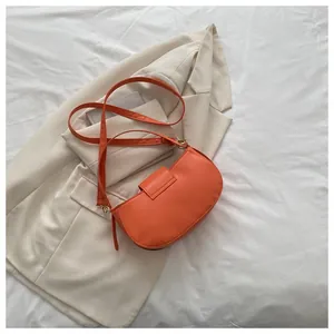 Detail view of orange saddle shoulder bag on beige blazer with smooth faux leather texture