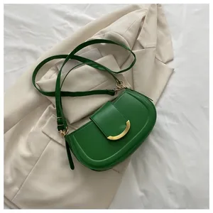 Detail shot of green saddle bag with gold buckle on beige blazer jacket background