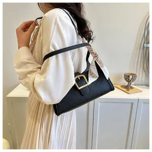 Detail of black quilted shoulder bag with gold buckle and decorative geometric silk scarf