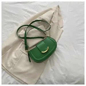Detail of a bright green saddle bag with golden crescent buckle on a beige blazer