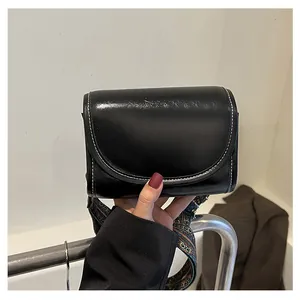 Détail du sac bandoulière en cuir noir avec surpiqûres blanches et large sangle colorée