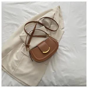 Close-up of brown crescent saddle bag with gold buckle on white blazer background