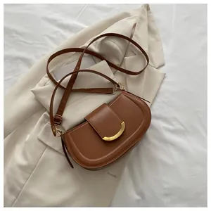 Detailed macro view of a brown saddle bag featuring a polished gold crescent moon buckle