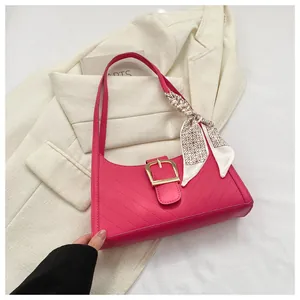 Close-up of rose red quilted handbag featuring a gold buckle and decorative silk scarf