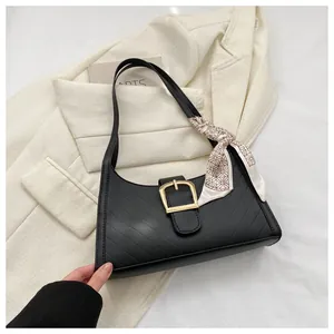 Detail of black quilted shoulder bag featuring gold buckle and chain print silk scarf