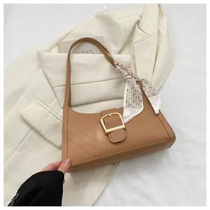 Detail of caramel leather handbag featuring twill texture, gold buckle, and silk scarf