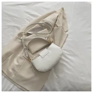 Detail of white saddle bag on beige blazer featuring gold hardware and smooth leather